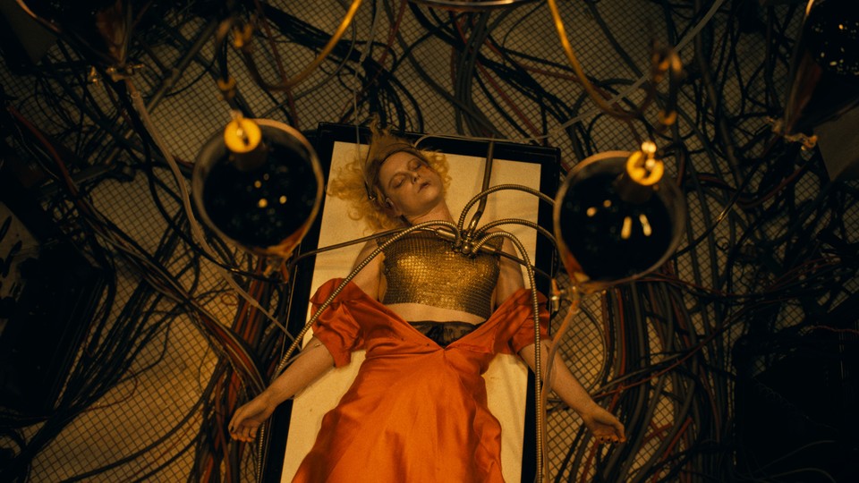 Jessie Buckley as Ida lies on a table surrounded by electrical cords, including some jutting out of her chest.