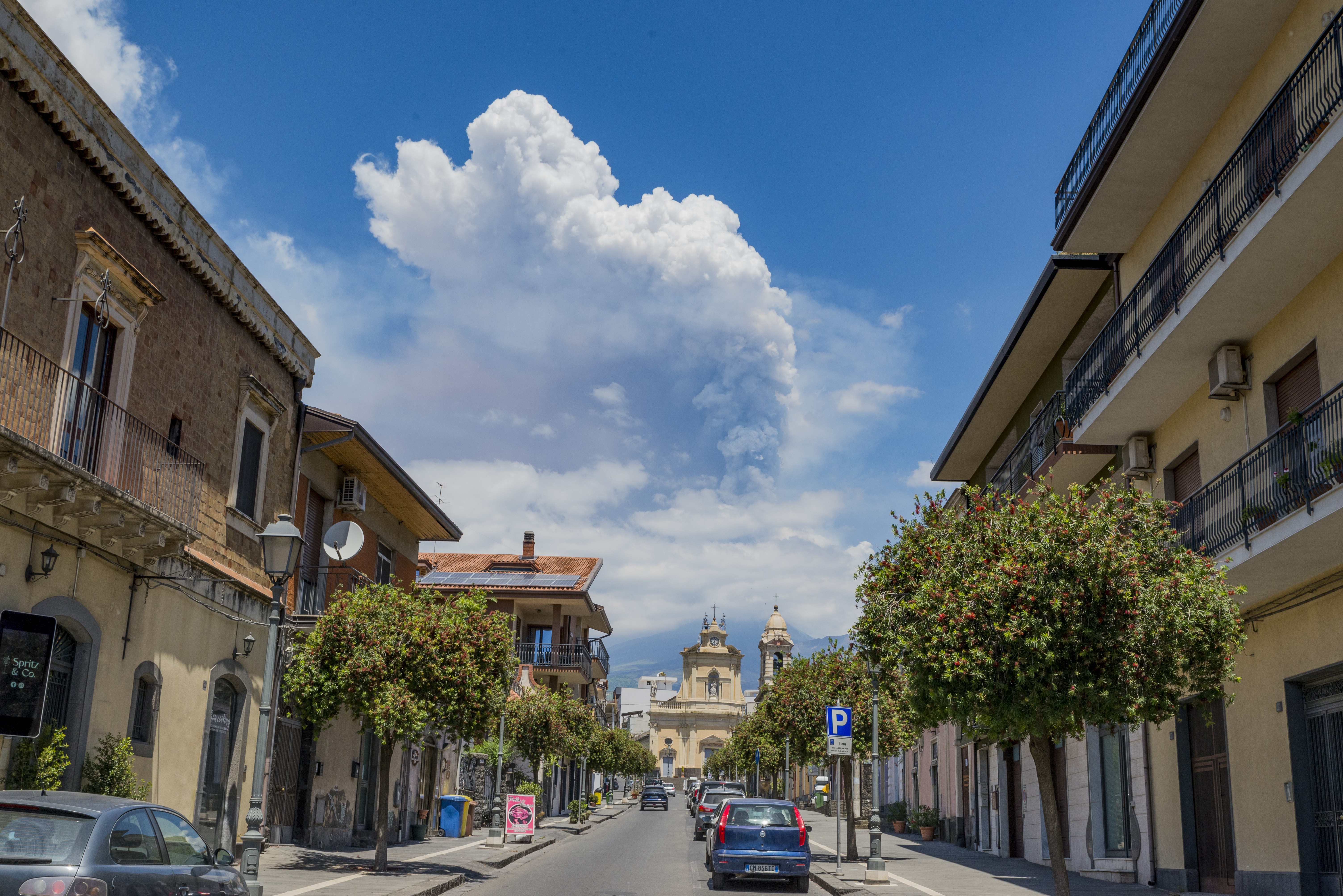 A cloud of ash and gas rises rises from a volcano, seen from a city street.