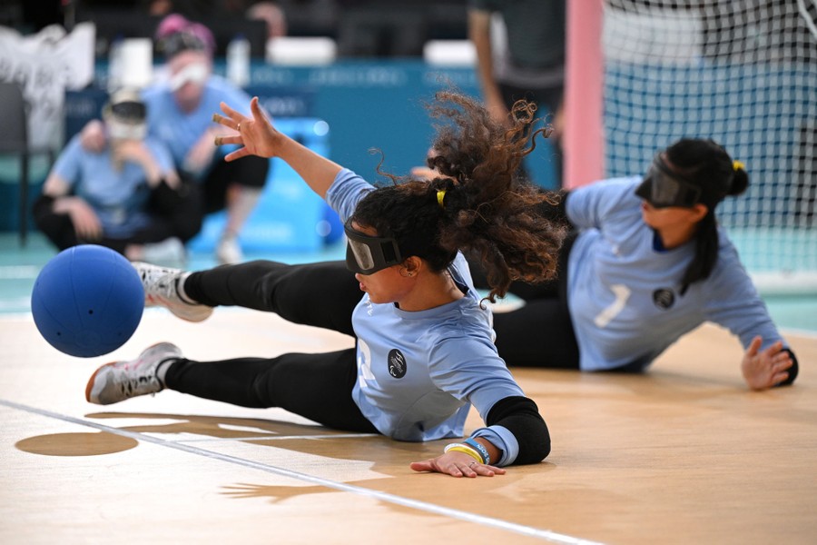 Two blindfolded goalball players stretch out to make a save during a match.