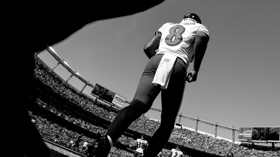 Black-and-white photo of football quarterback No. 8 poised to start running in crowded stadium
