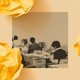 A black and white photo shows three desks in a row inside an office. A woman sits working at each desk