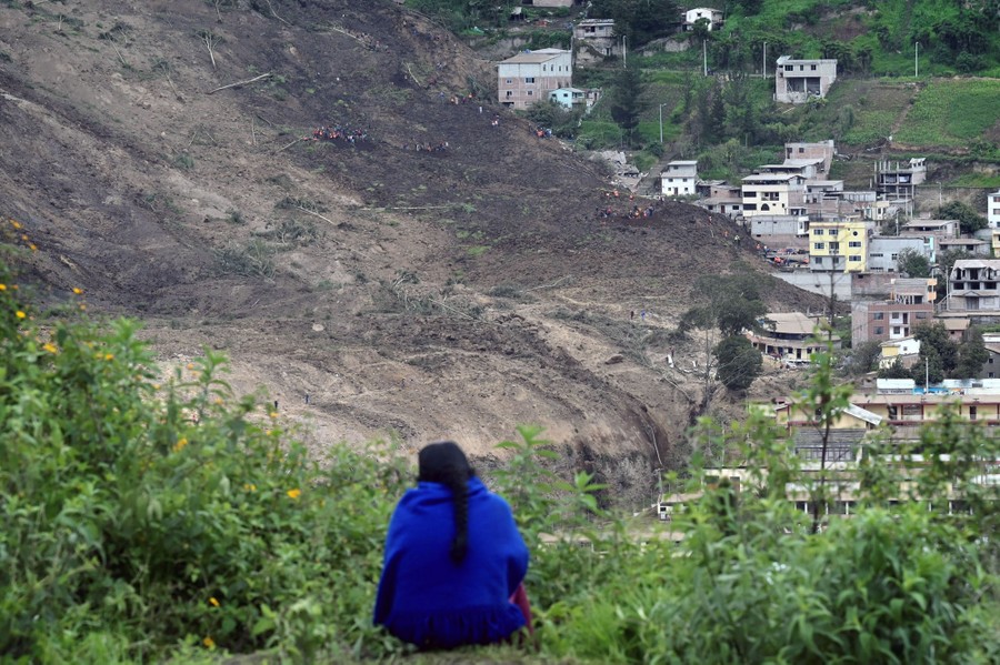 A person sits, overlooking a large landslide that has run into a residential area.