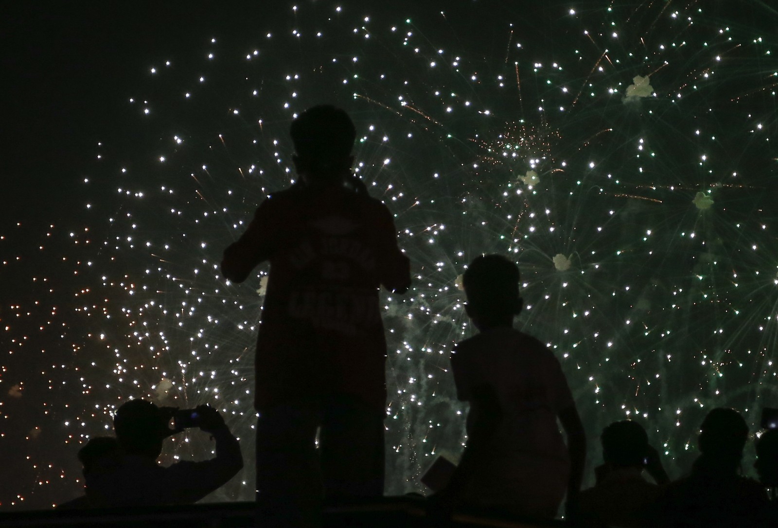 People look up toward the night sky as sparks fall from a fireworks display.