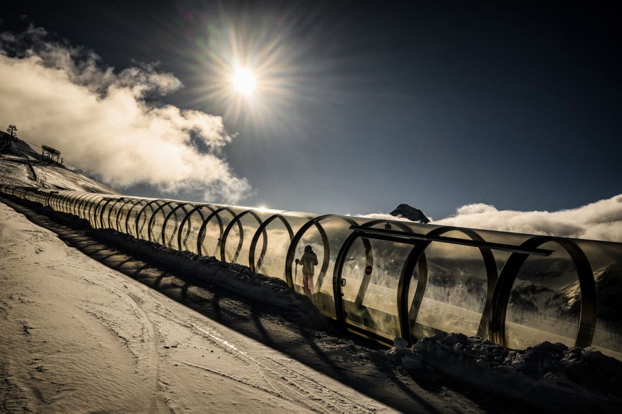 A person rides a ski lift inside a plexiglass tube on a slope.