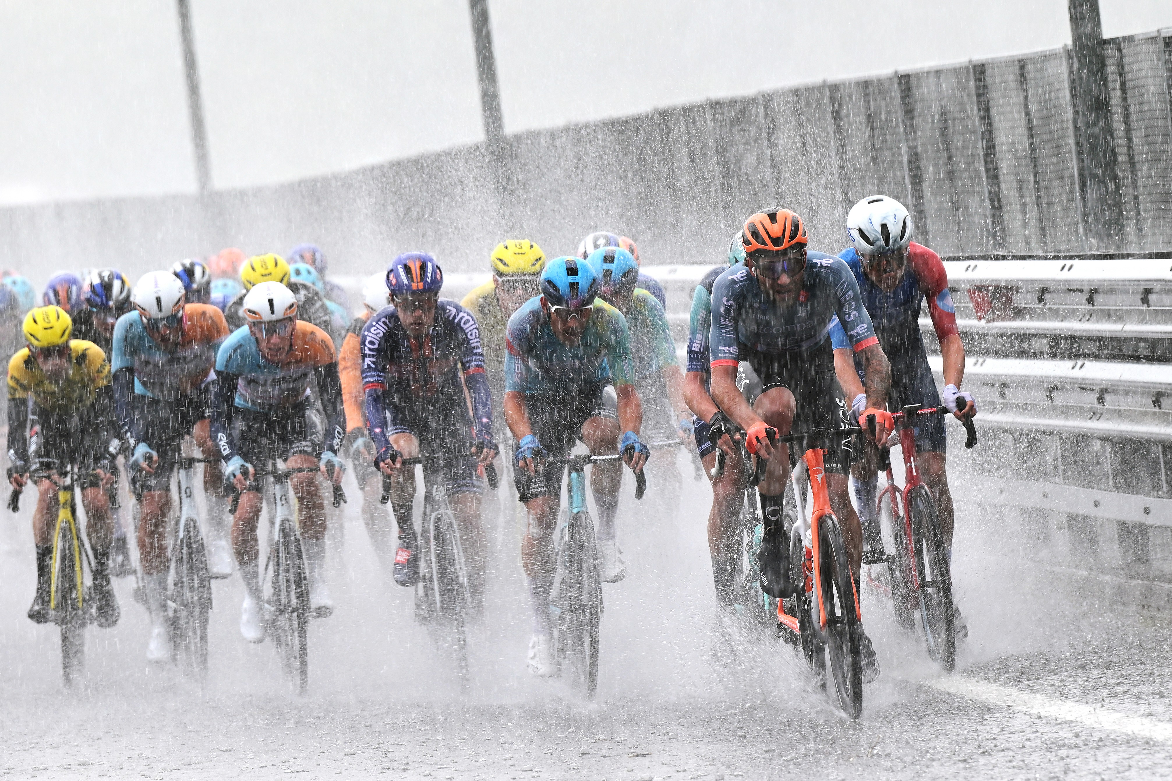 A group of racing cyclists ride through heavy rain.