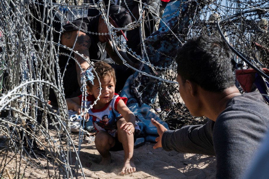 A young boy crawls through concertina wire toward an adult at the Mexico-U.S. border.