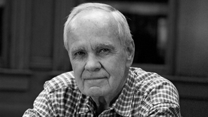 black-and-white sketch of Cormac McCarthy's face looking to one side with inset image of two people embracing in waves