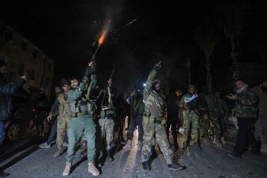 Soldiers stand in a street, shouting and firing weapons in the air.