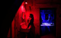 Two people are seen in separate rooms, one lit by a blue light, the other by a red light.