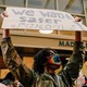 A young man wearing a rainbow mask holds up a sign that says "We want safer schools." In the crowd behind him, other signs read: "CPS Listen to Us" and "Student Voices Matter"