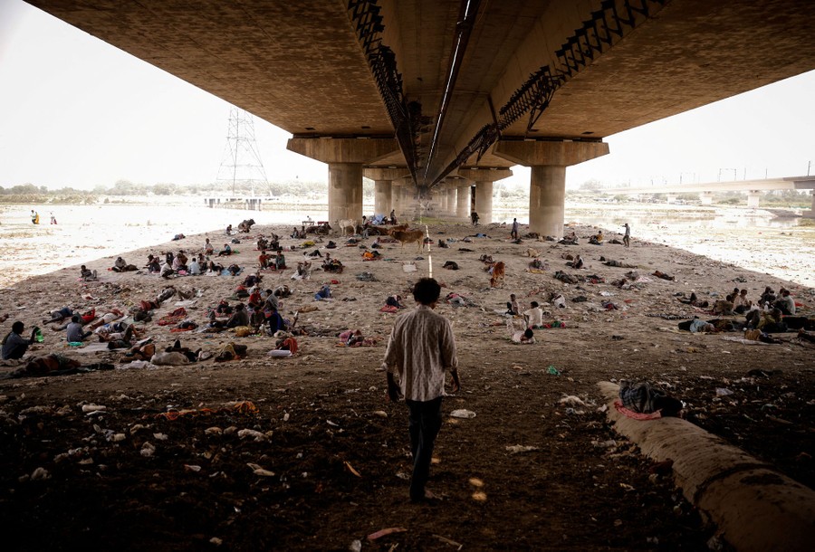 Dozens of people sit and lie on the ground beneath a road bridge.