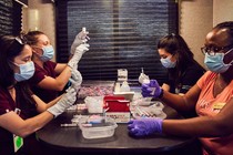 Four people sit filling vials with vaccine using syringes.