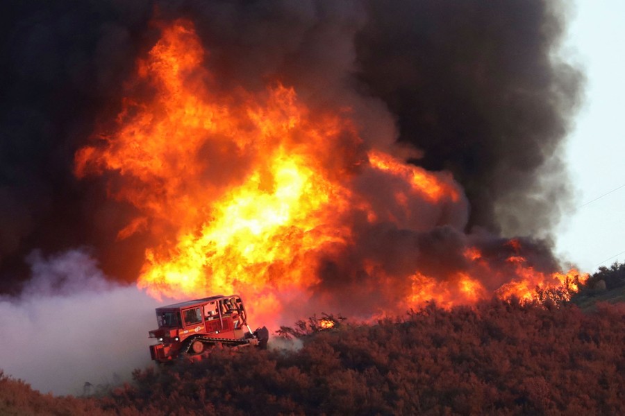 A bulldozer works along the edge of a brush fire.