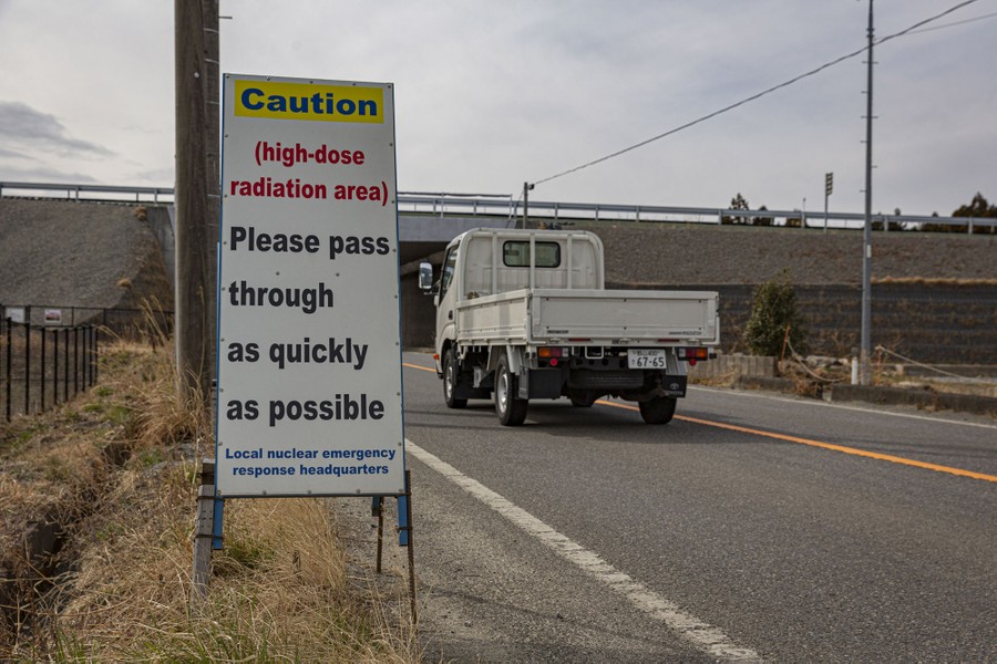 A roadside sign reads: "Caution (high-dose radiation area) Please pass through as quickly as possible."