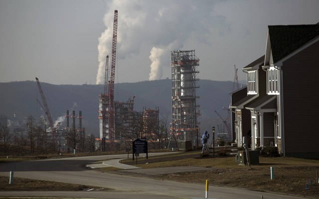 A smoking fracking project sits behind a suburban subdivision and beneath a gray, smoggy sky.
