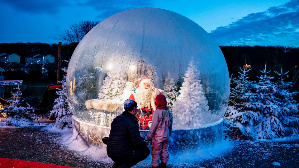 A parent and child stand in front of a blow-up snowglobe.