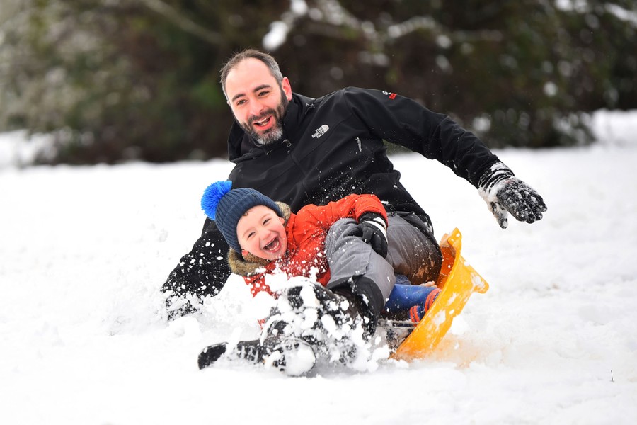 A child and adult fall from a sled while laughing.