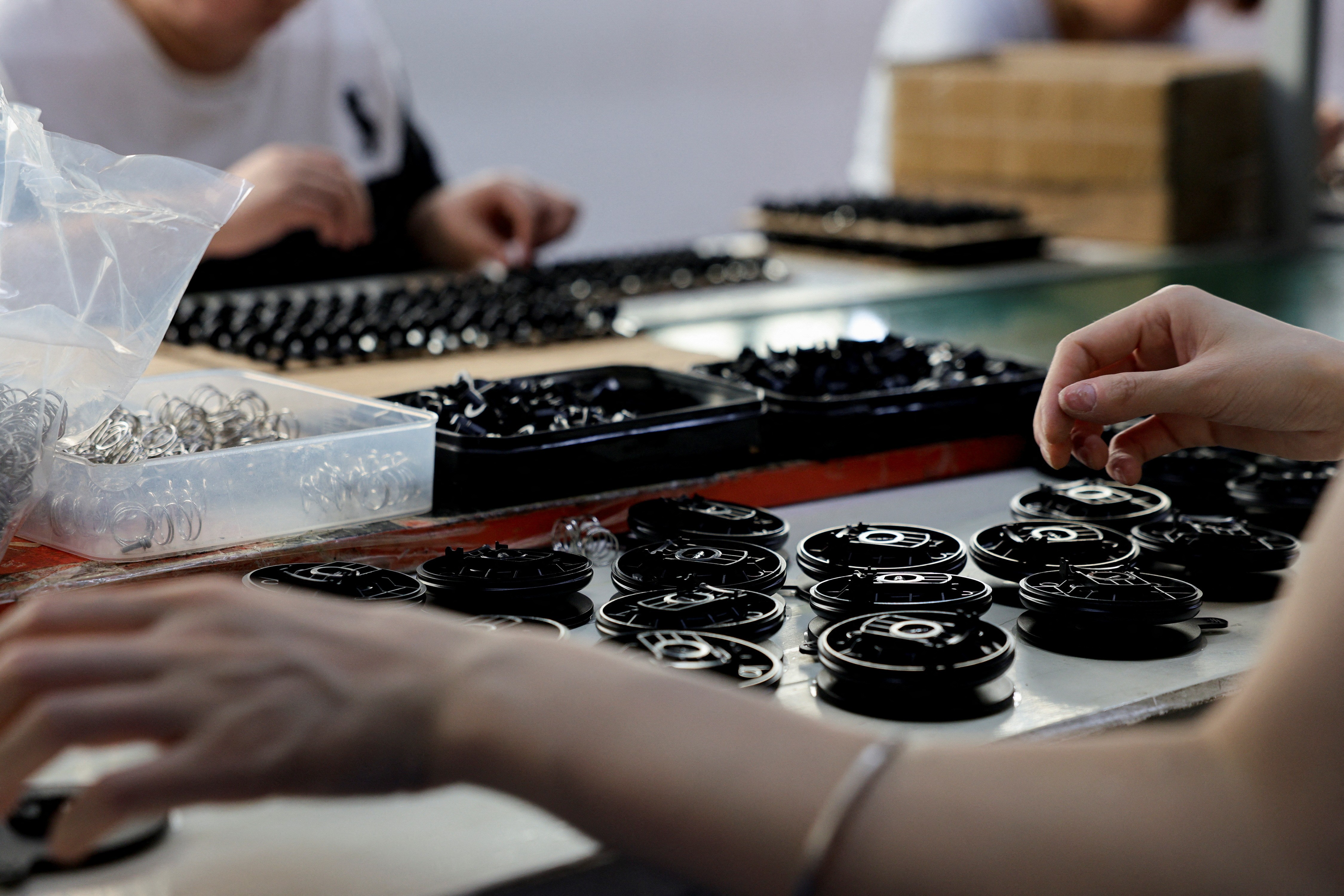 Employees work at a table on an assembly line producing car smartphone holders.