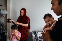 A mom ties her daughter's hair into a ponytail while a father holds their son.