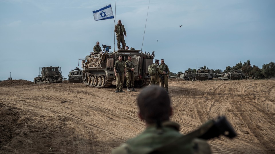 In the desert near the Israel-Gaza border, a tank with soldiers atop and alongside flies the Israeli flag.