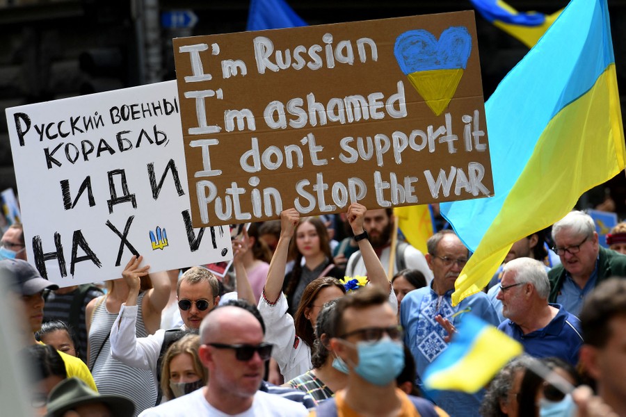 A crowd of people holds flags and signs including one that reads "I am Russian, I am ashamed, I don't support it, Putin stop the war. "