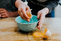 A picture of someone cracking an egg on a bowl but spilling the yolk onto a table