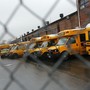School buses photographed through a chain-link fence.