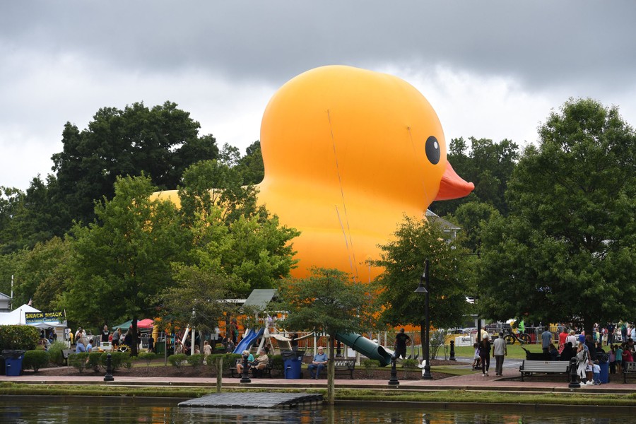 A huge inflatable yellow duck sits in a park among trees.