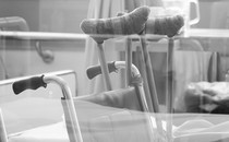 Black-and-white photo of crutches and a wheelchair in what seems to be a hospital