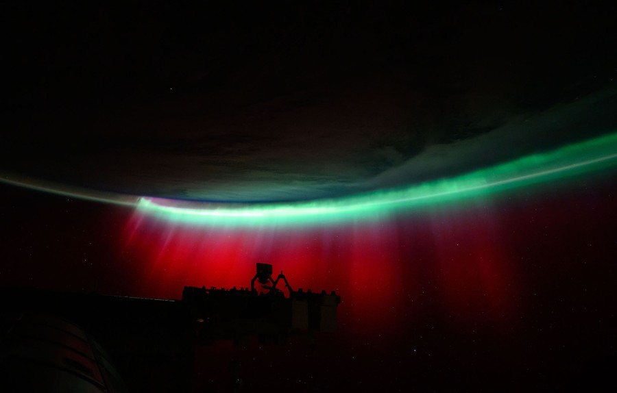 Part of the International Space Station is silhouetted against a colorful aurora