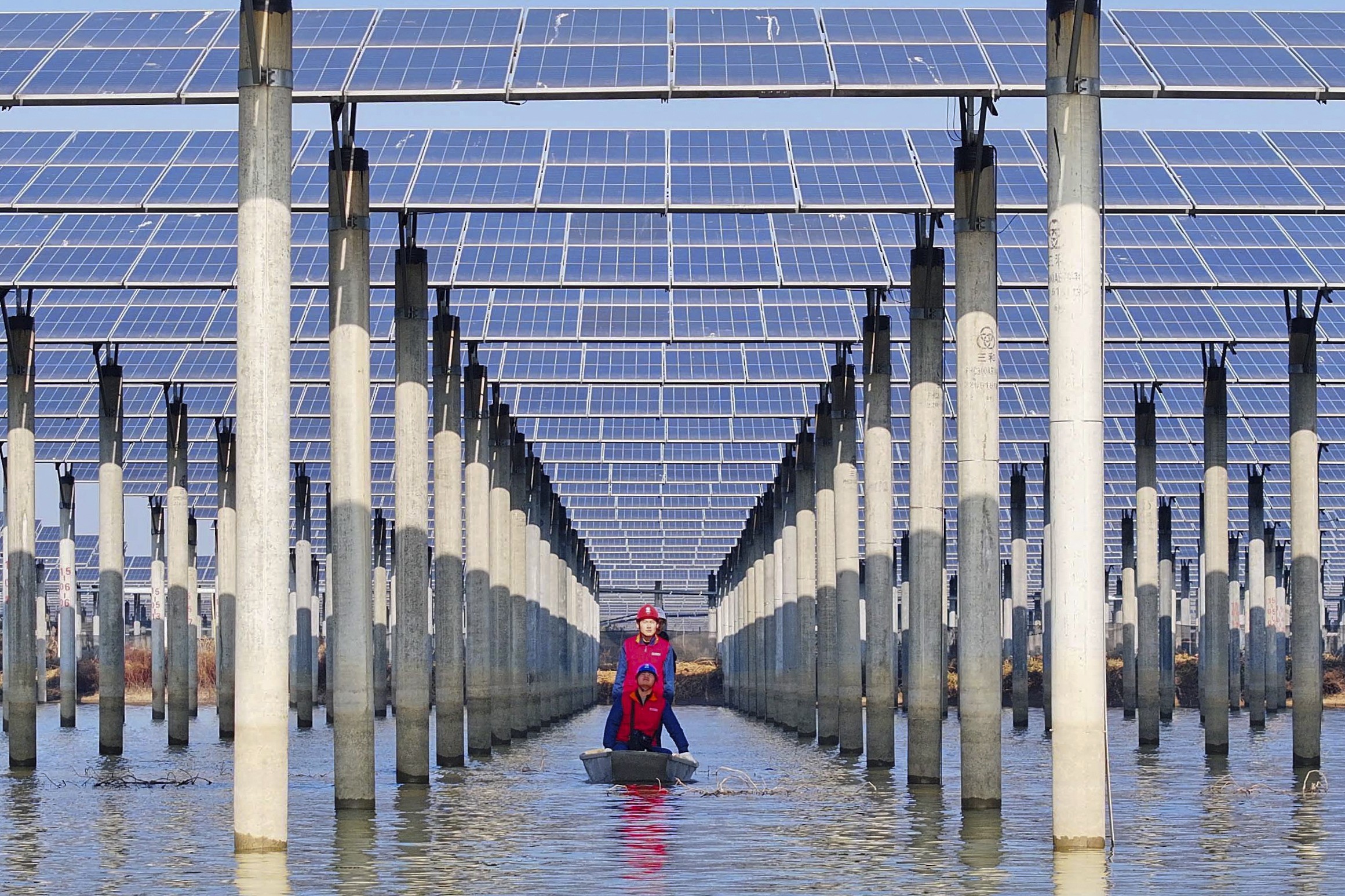 Three workers in a small boat check solar panels installed above a lake.