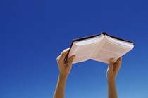 Young woman holding book up in air, low angle view