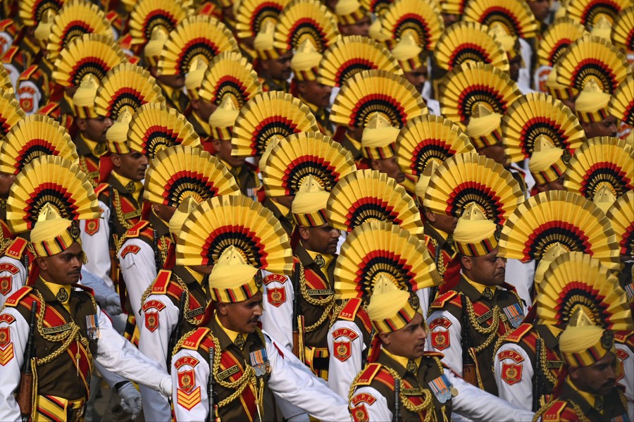 Soldiers march wearing dress uniforms with crested headgear.