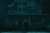 man in a suit stands in front of a spooky house at night