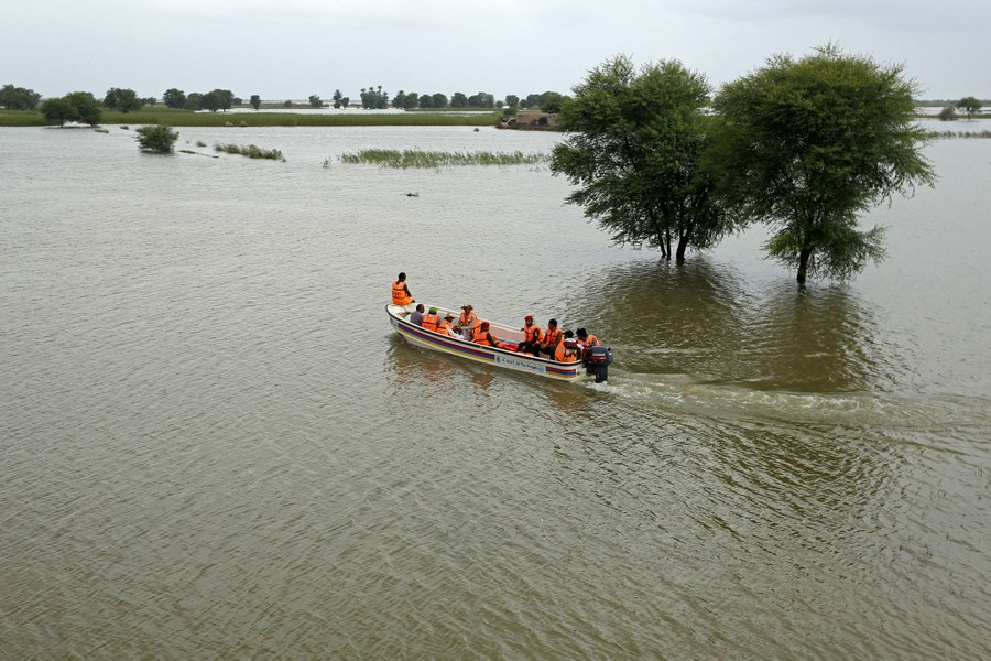 About 10 people ride in a small motorboat through a wide flooded plain.