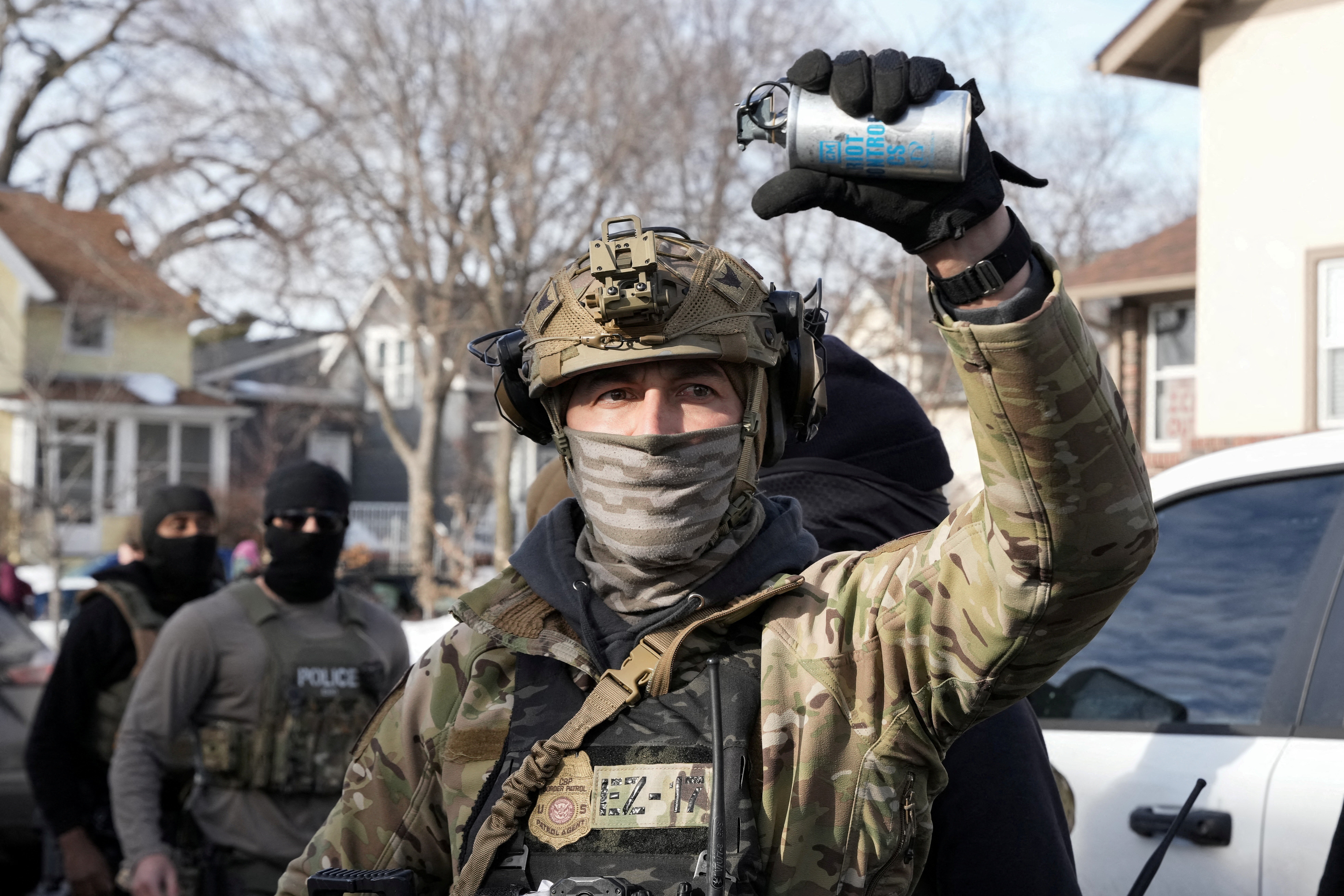 A federal agent holds up a riot control tear gas grenade, while standing in a residential street.