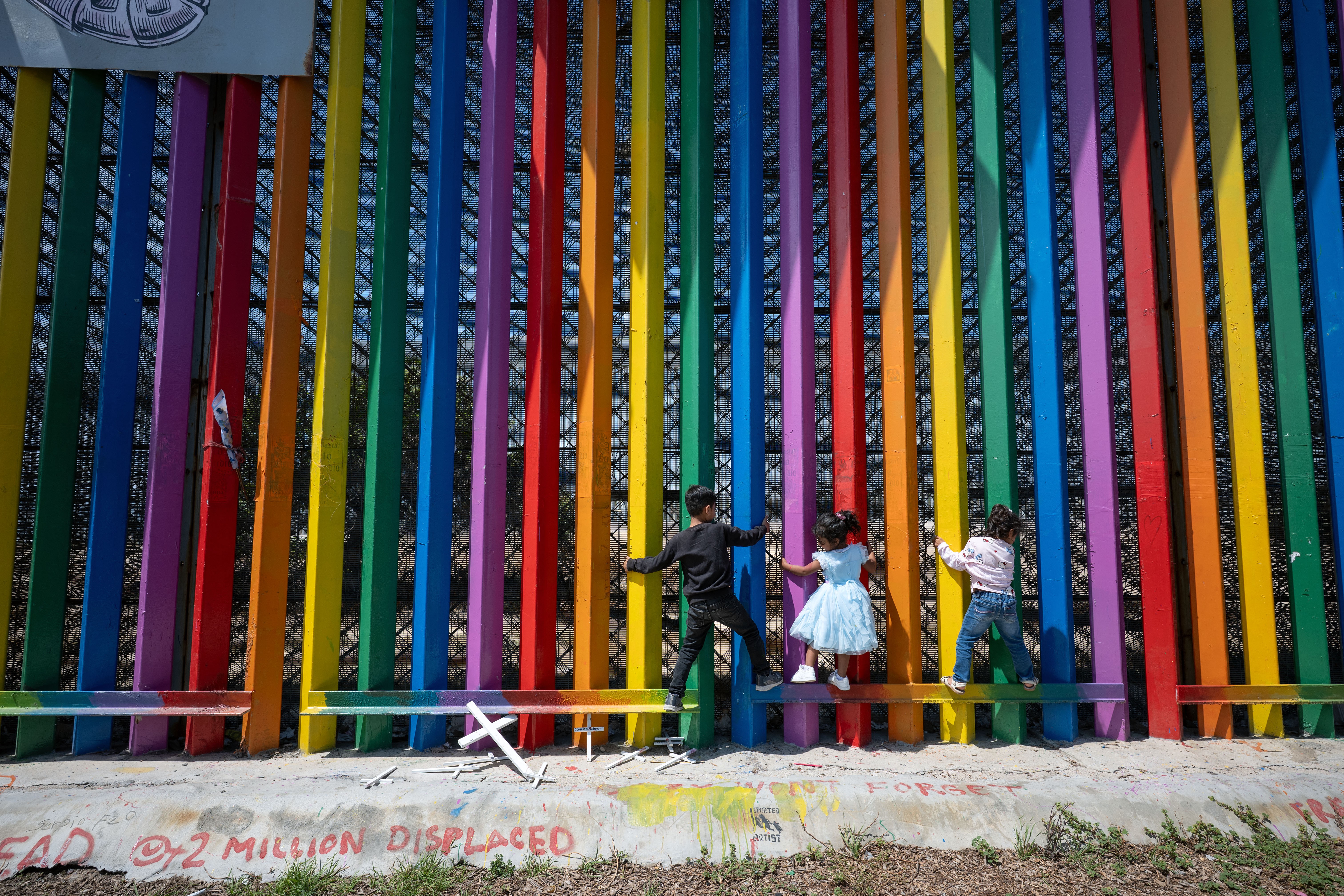 Children play, climbing the Mexico-U.S. border wall that has been painted in a rainbow of colors.