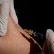 a gloved hand injecting a needle into an arm
