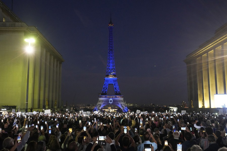 The Eiffel Tower is illuminated with the colors of Israel, surrounded by a crowd holding up their illuminated phones.