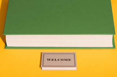 A smaller book that says "WELCOME" spread out in front of a larger book like a welcome mat