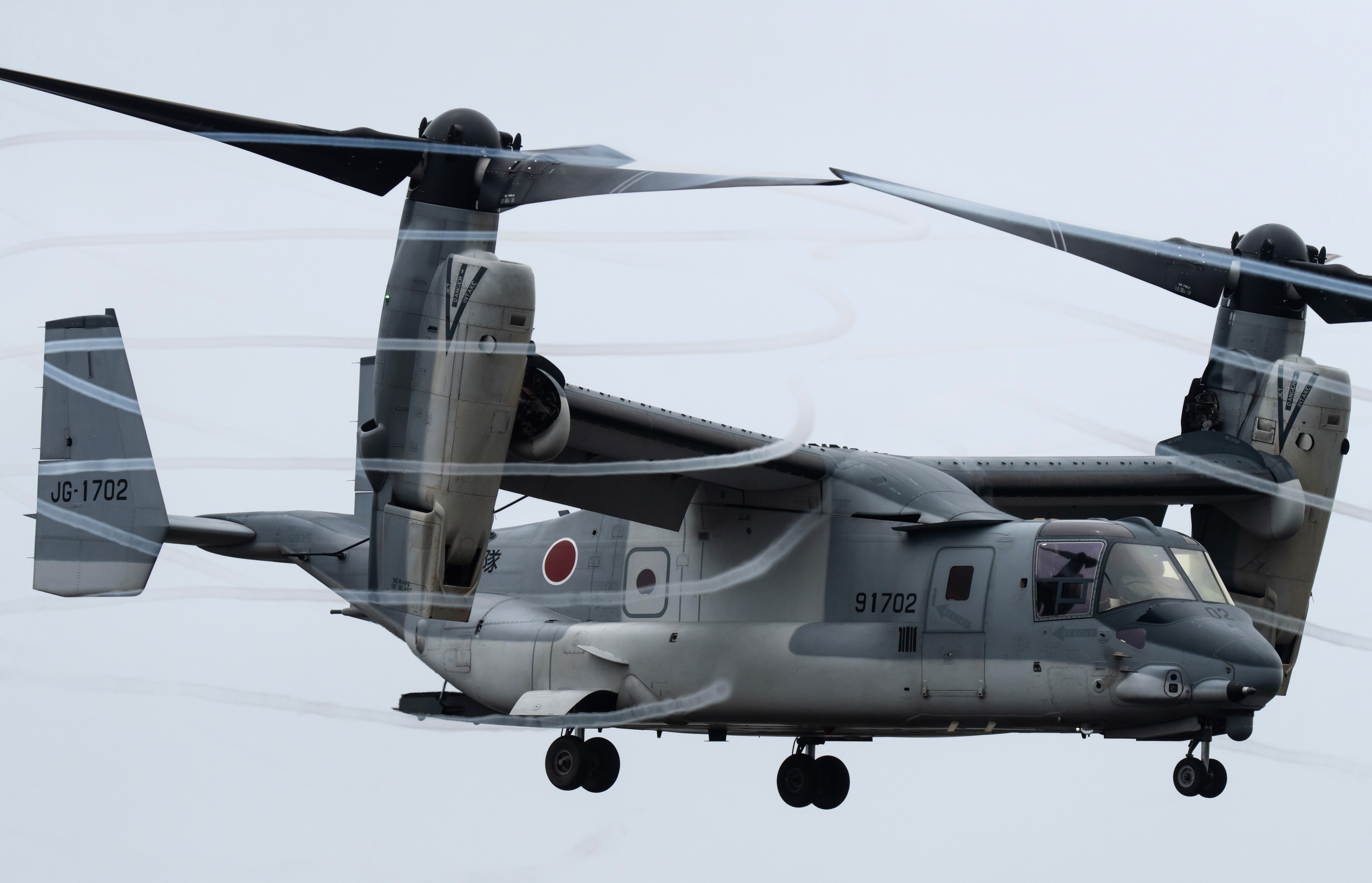 Two sets of vortices swirl in the air as a twin-rotor V-22 Osprey aircraft flies.