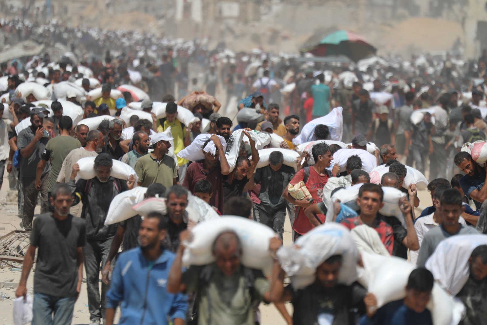 Long lines of mostly men carry heavy sacks of food.