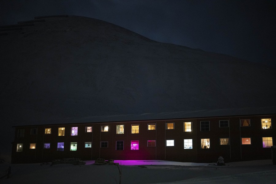 Multicolored windows of a long building light up at night in an Arctic setting.
