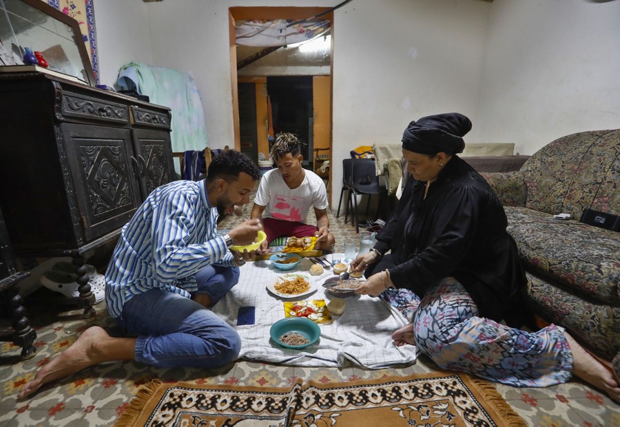 A family of three shares a meal while seated on the floor of a living room.