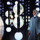 A person stands inside a dark room, looking at suspended globes, lit up in an exhibition.