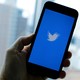 A hand hold a phone with the twitter logo on the screen in blue and white.