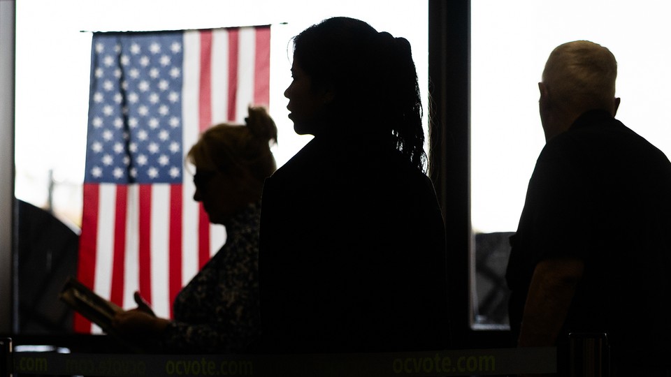 Voter are silhouetted near the American flag while voting in the California Statewide Special Election at the Huntington Beach Central Library in Huntington Beach Tuesday, Nov. 4, 2025.