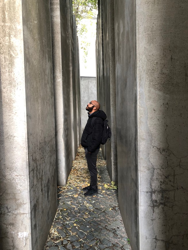 photo: man with backpack stands in narrow passage between tall concrete columns and looks up