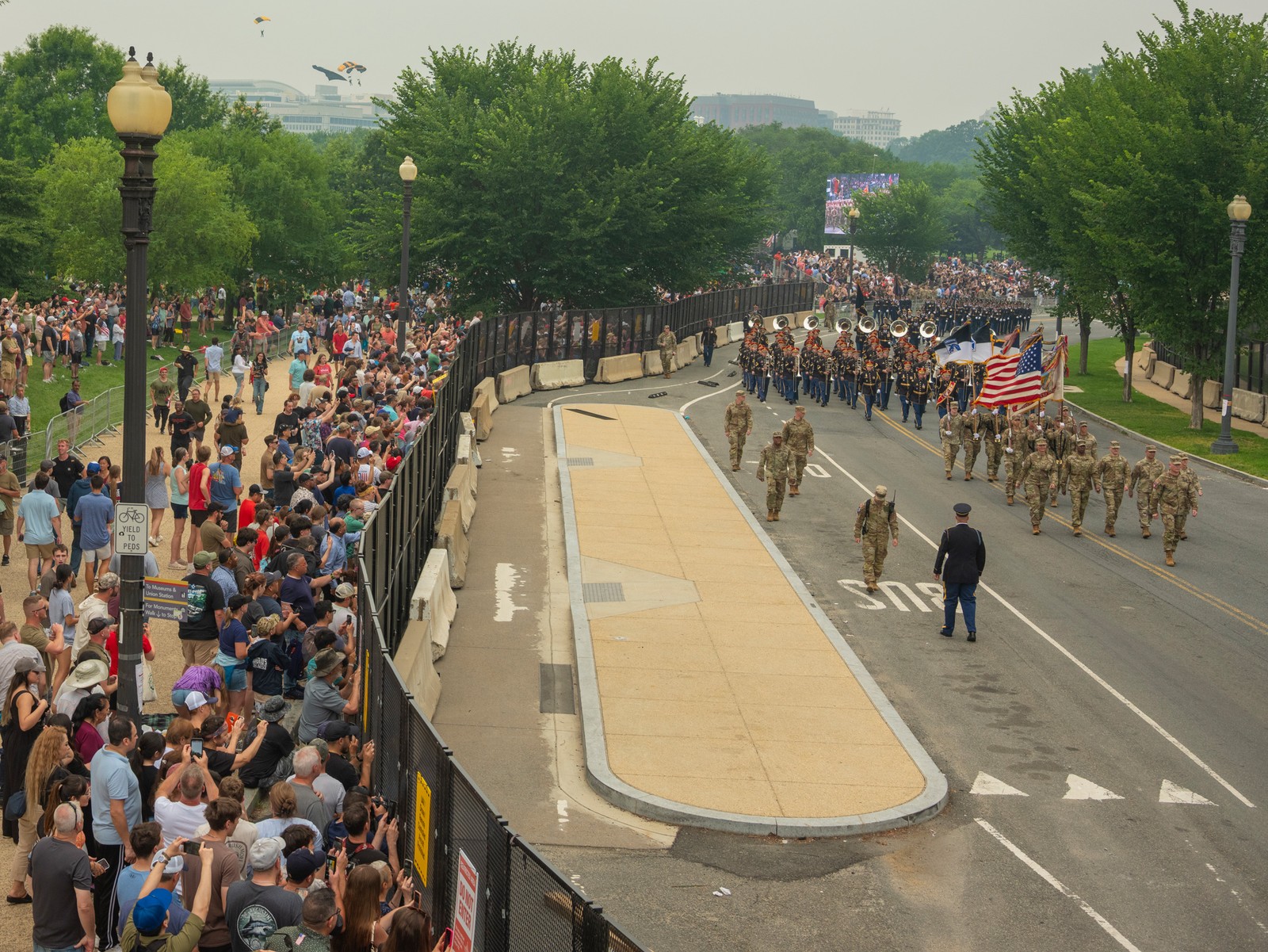 Picture of the parade proceeding along the National Mall while parachuters from the Army Golden Knights descend onto the White House ellipse to present President Trump with a folded American flag.