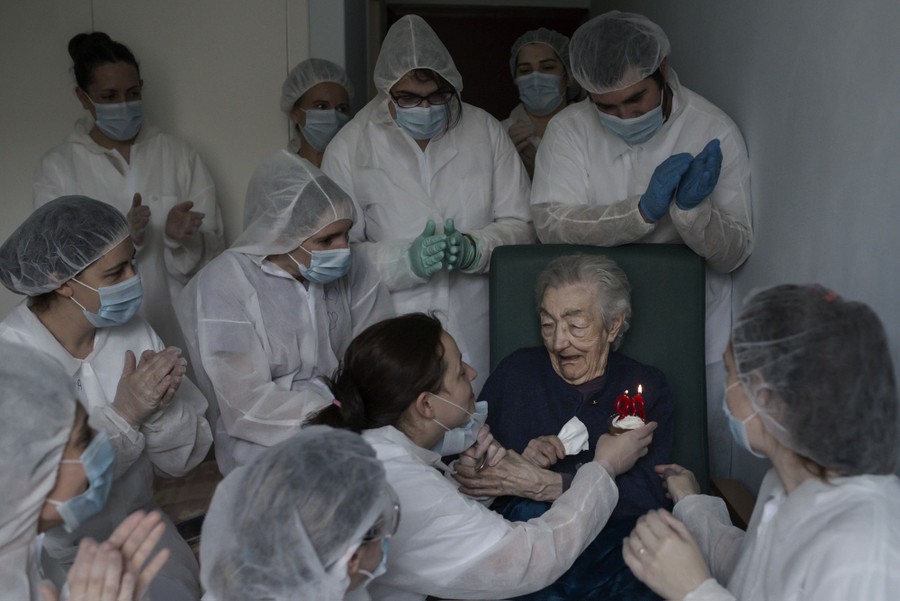 People wearing protective gear gather around an elderly person to celebrate a birthday.